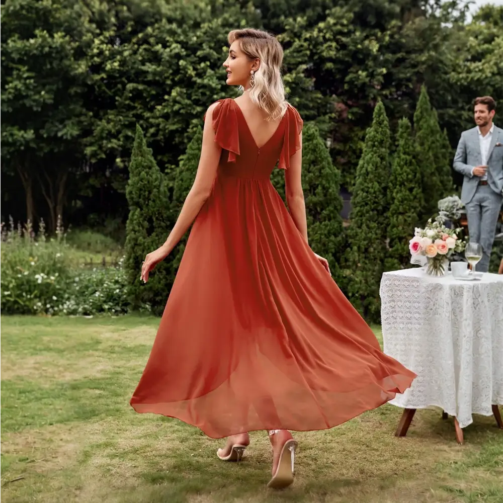 Vue de dos d'une élégante robe cocktail chic originale en terracotta, avec un décolleté en V et une coupe fluide, portée par une femme blonde dans un jardin verdoyant.