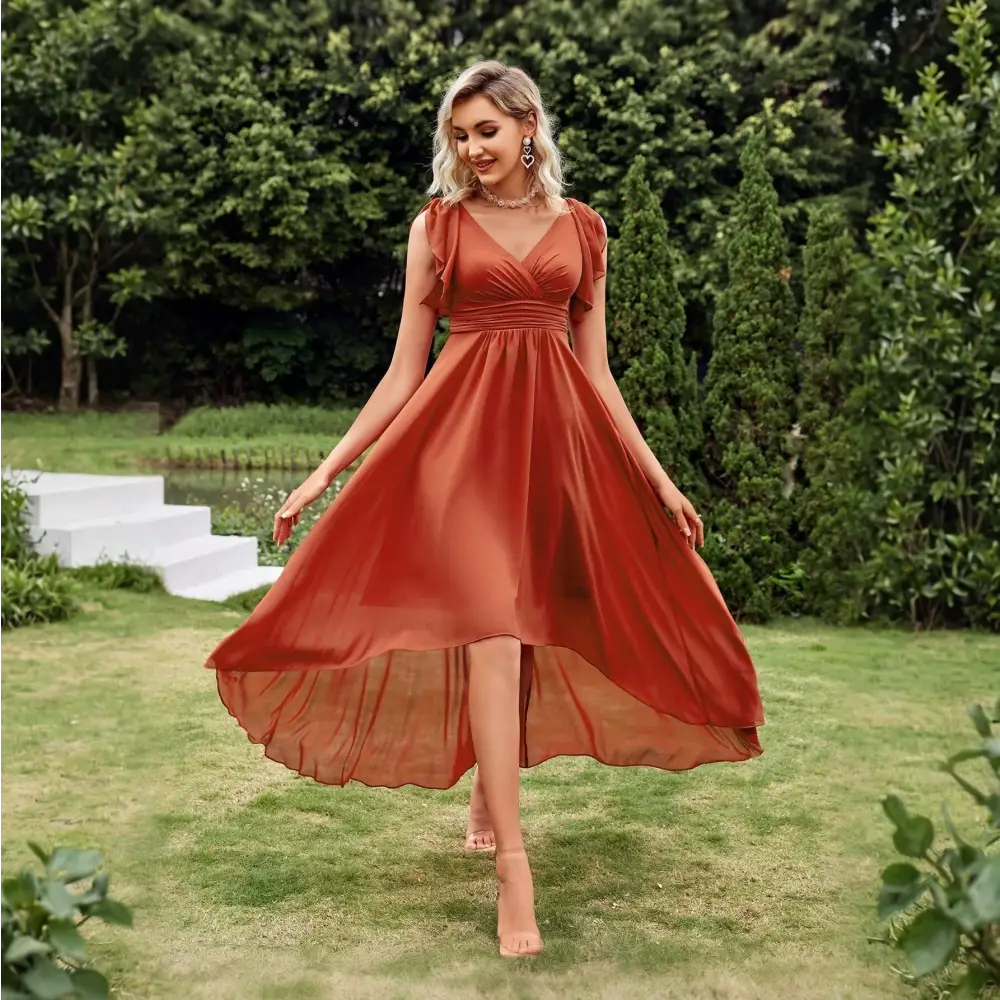 Vue de face d'une robe cocktail chic originale en terracotta, avec un décolleté en V et une coupe asymétrique, portée par une femme blonde dans un cadre extérieur élégant.