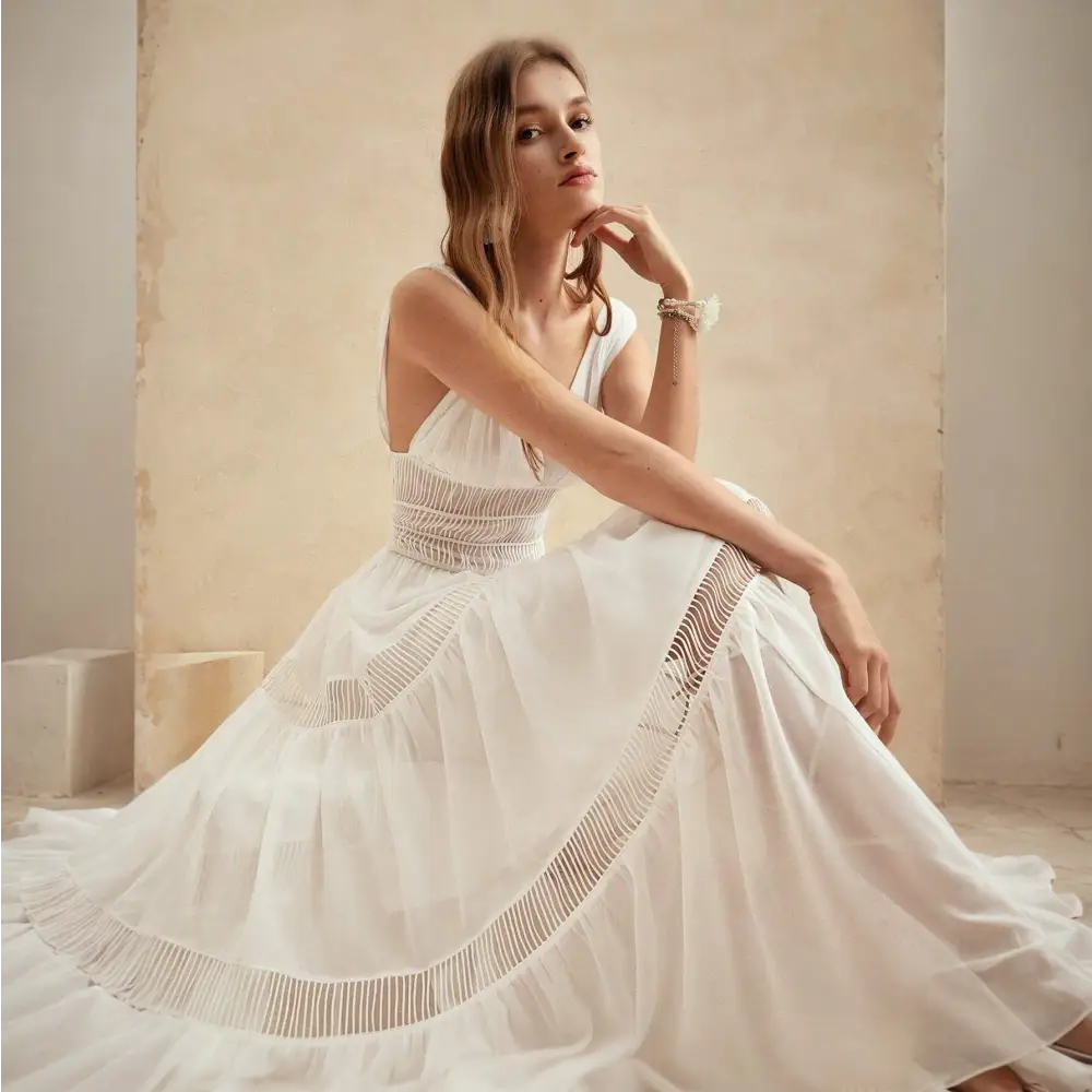 Une robe cocktail longue en soie blanche, portée par un modèle assis, mettant en avant les détails délicats en dentelle et la fluidité du tissu pour une allure élégante et raffinée.