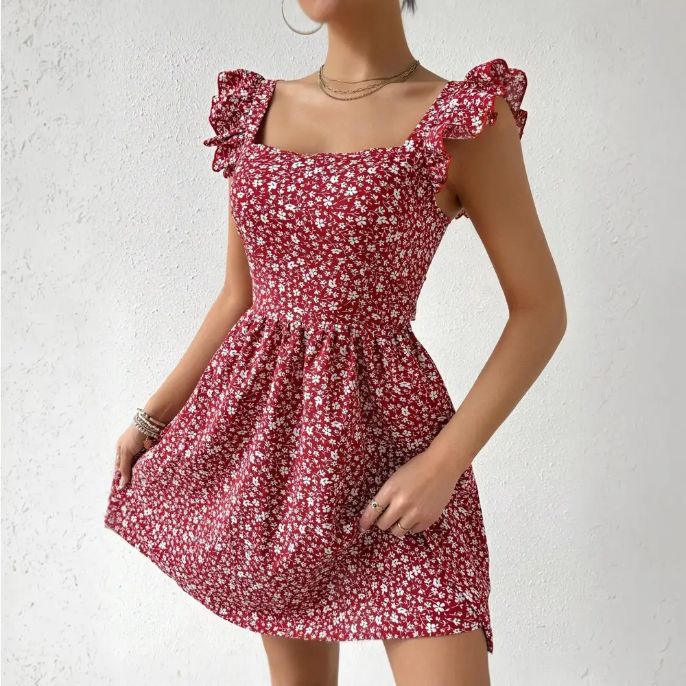 Une femme portant une robe cocktail rouge à motifs floraux blancs. La robe a un décolleté carré et des manches à volants. La femme pose les mains sur les hanches, mettant en valeur les détails de la robe.