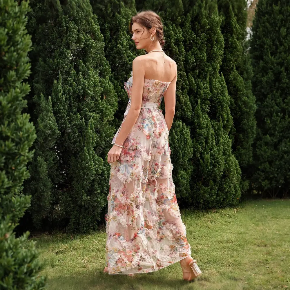 Vue de dos d'une élégante robe cocktail mariage bohème chic, avec un imprimé floral délicat, sans bretelles et ceinturée à la taille, portée par une femme dans un jardin verdoyant.