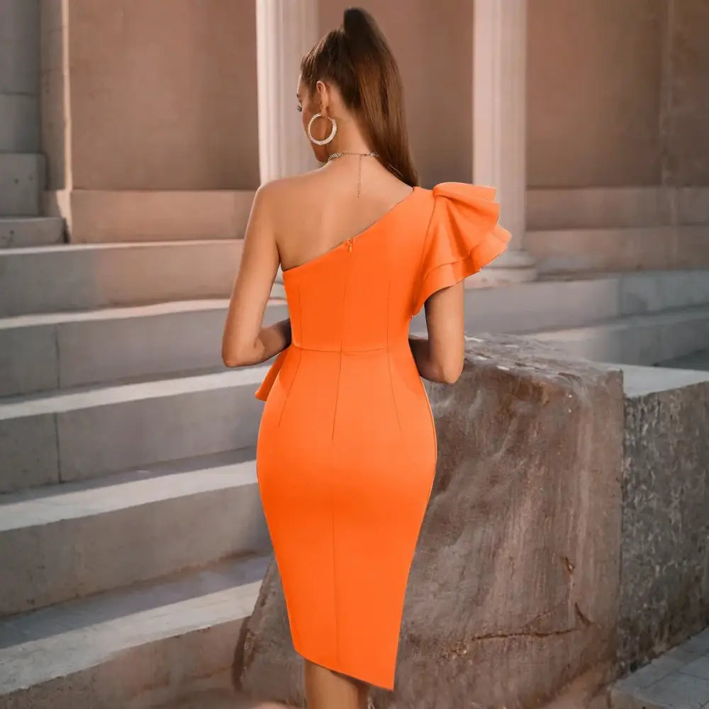 Vue arrière de la robe cocktail orange. La robe présente une coupe asymétrique avec une seule épaule ornée d’un grand volant. Le dos est lisse avec une fermeture éclair centrale, mettant en valeur la silhouette du mannequin. Le décor avec des colonnes en arrière-plan ajoute une touche classique et élégante à l’ensemble.