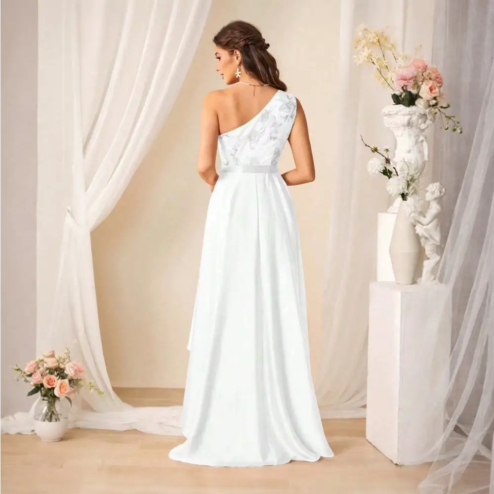 Femme portant une robe de cocktail longue blanche, vue de dos, avec une épaule dénudée et des motifs floraux.