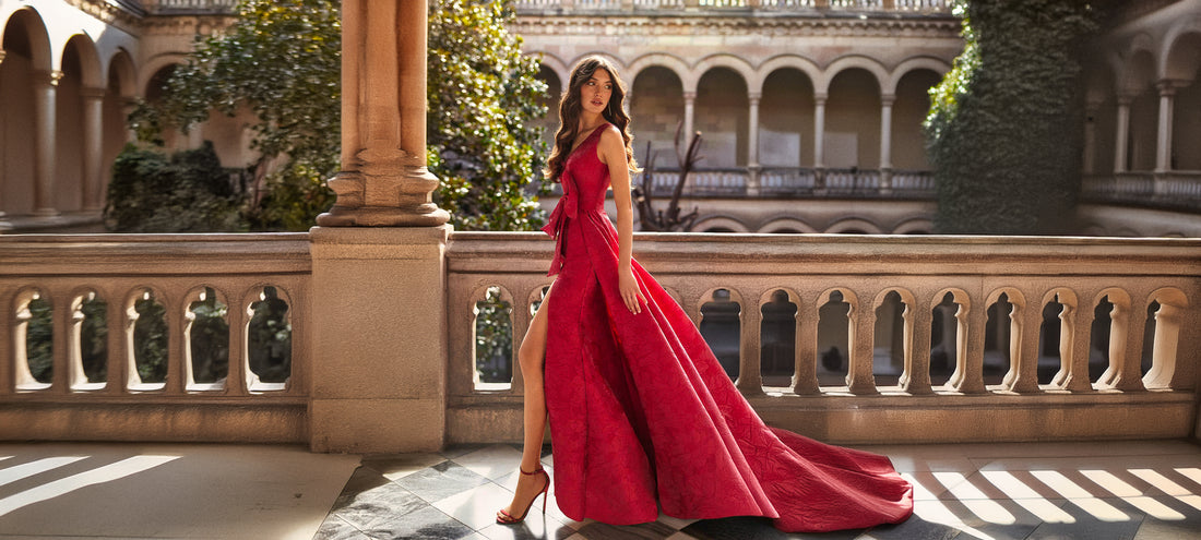 Une femme portant une robe cocktail longue rouge avec un motif floral subtil, posant dans un cadre architectural 