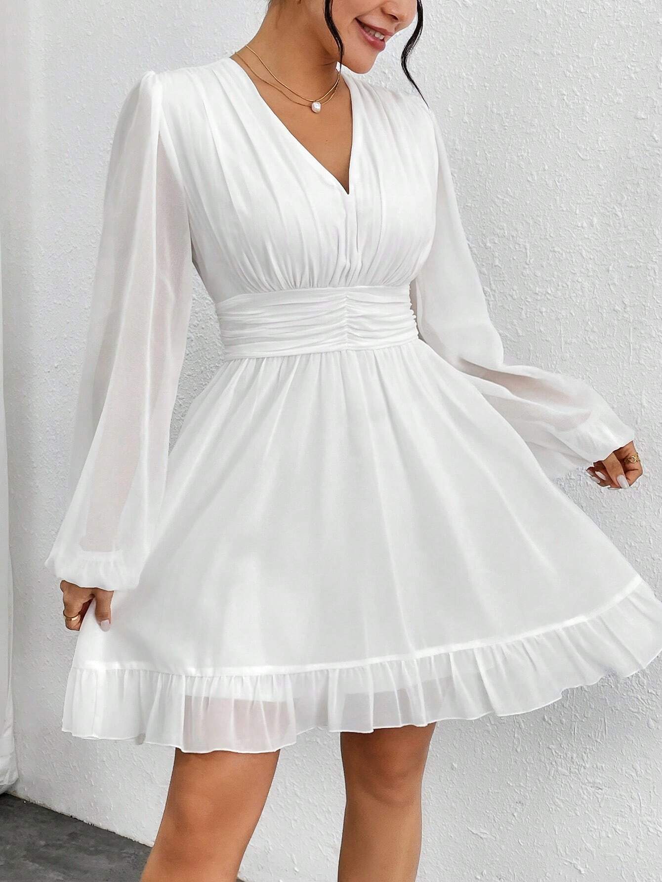 Une charmante robe cocktail blanche vue de face, mettant en valeur un décolleté en V, des manches ¾ fluides, et une ceinture froncée à la taille pour une silhouette élégante.