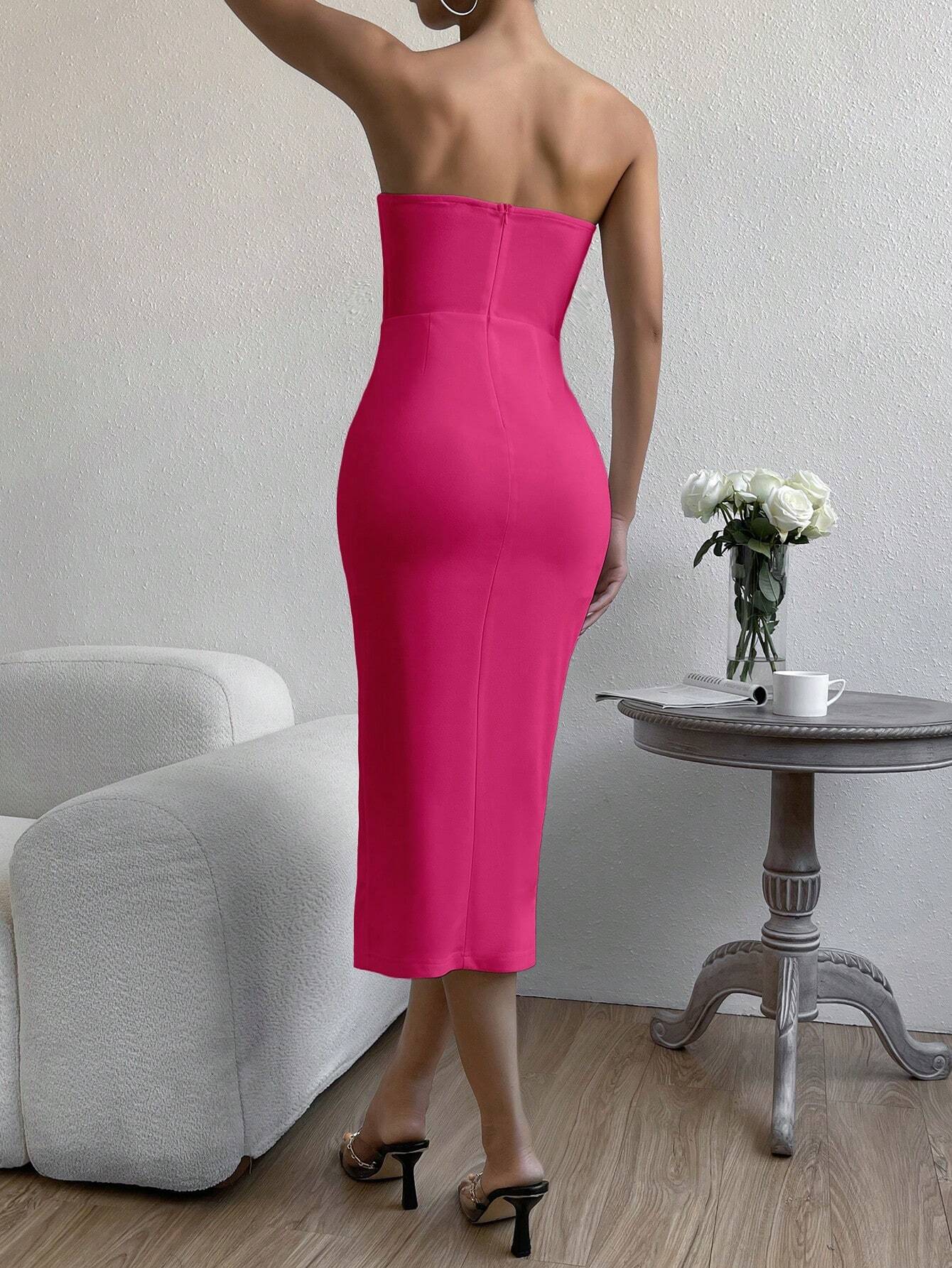 Vue de dos d’une femme portant une robe cocktail bustier rose fuchsia, debout à côté d’une table en bois.