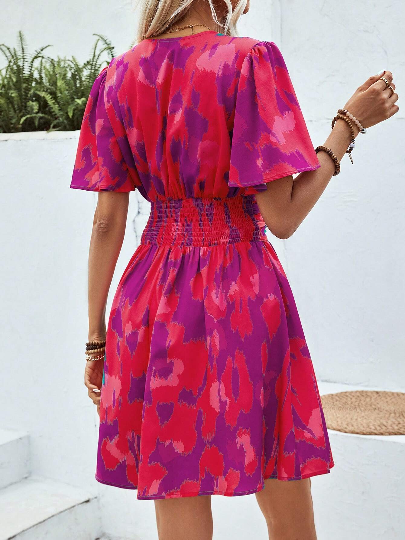 Vue de dos d'une robe cocktail chic et originale, avec un motif abstrait rose et violet, une ceinture élastique à la taille et des manches courtes flottantes, portée par une femme blonde.