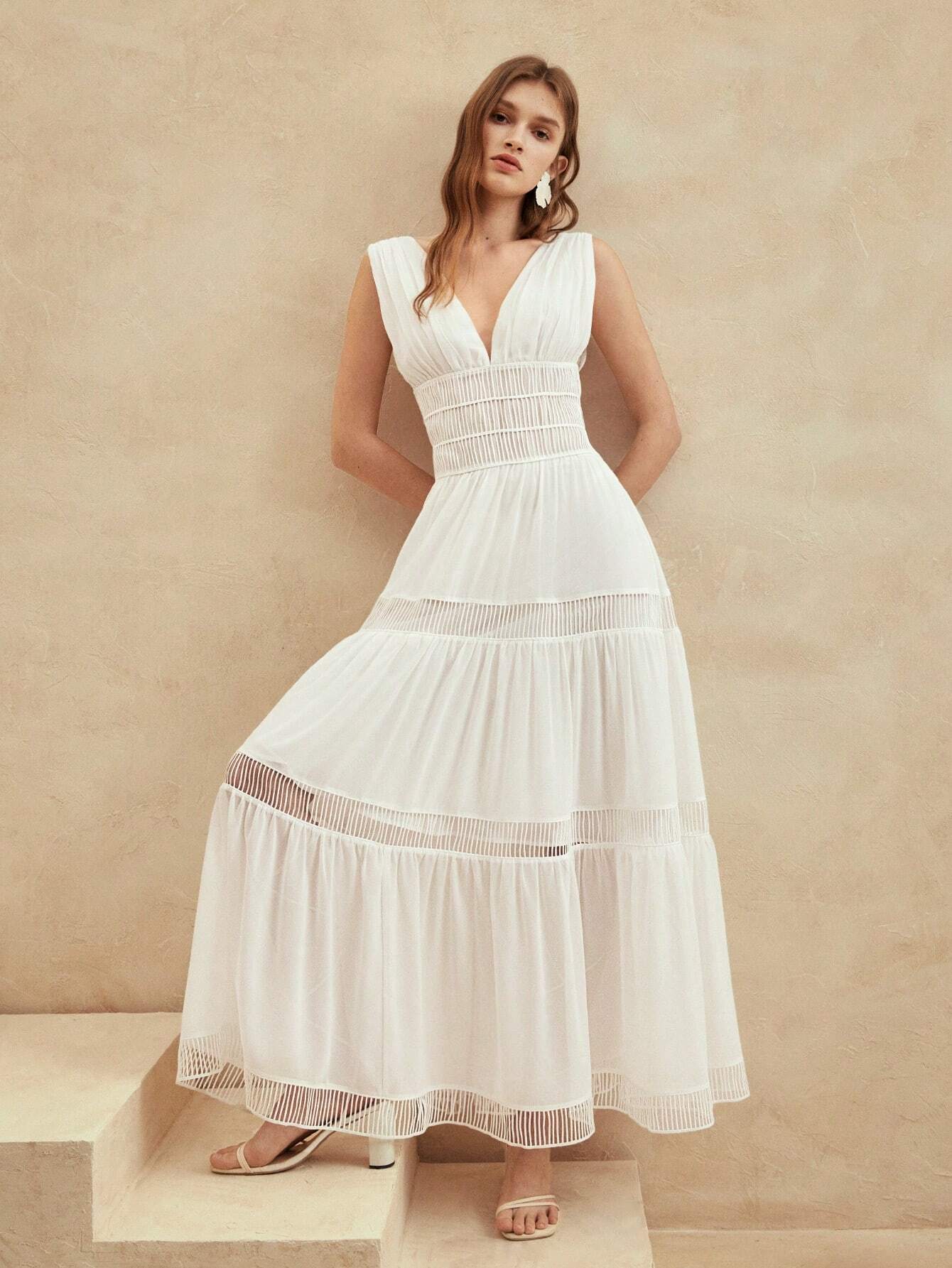 Une robe cocktail longue en soie blanche vue de trois quarts, avec un décolleté en V profond, une coupe fluide et des détails en dentelle, parfaite pour une soirée chic et élégante.