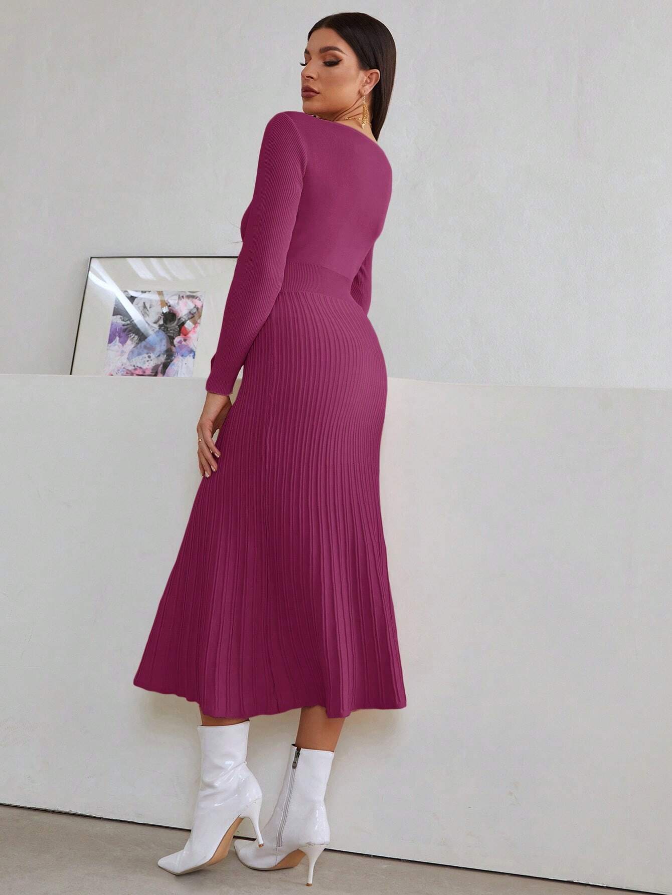 Vue de dos d’une femme portant une robe de cocktail hiver en tricot violet. La robe a des manches longues et une jupe plissée. La femme est accessoirisée avec des boucles d’oreilles dorées et des bottes blanches. Elle pose de dos, mettant en valeur la silhouette de la robe.