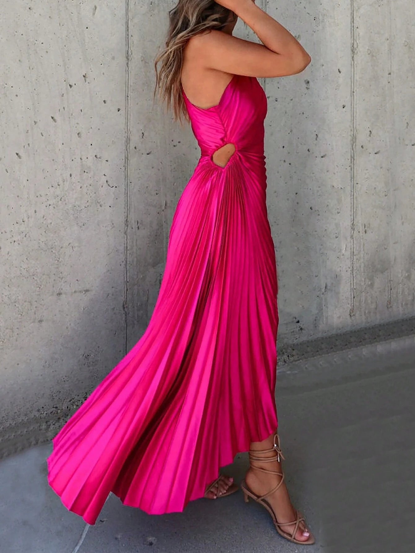 Une robe cocktail satin de couleur fuchsia vue de profil. La robe est sans manches, présente des plis élégants et une coupe asymétrique avec une ouverture sur le côté de la taille.