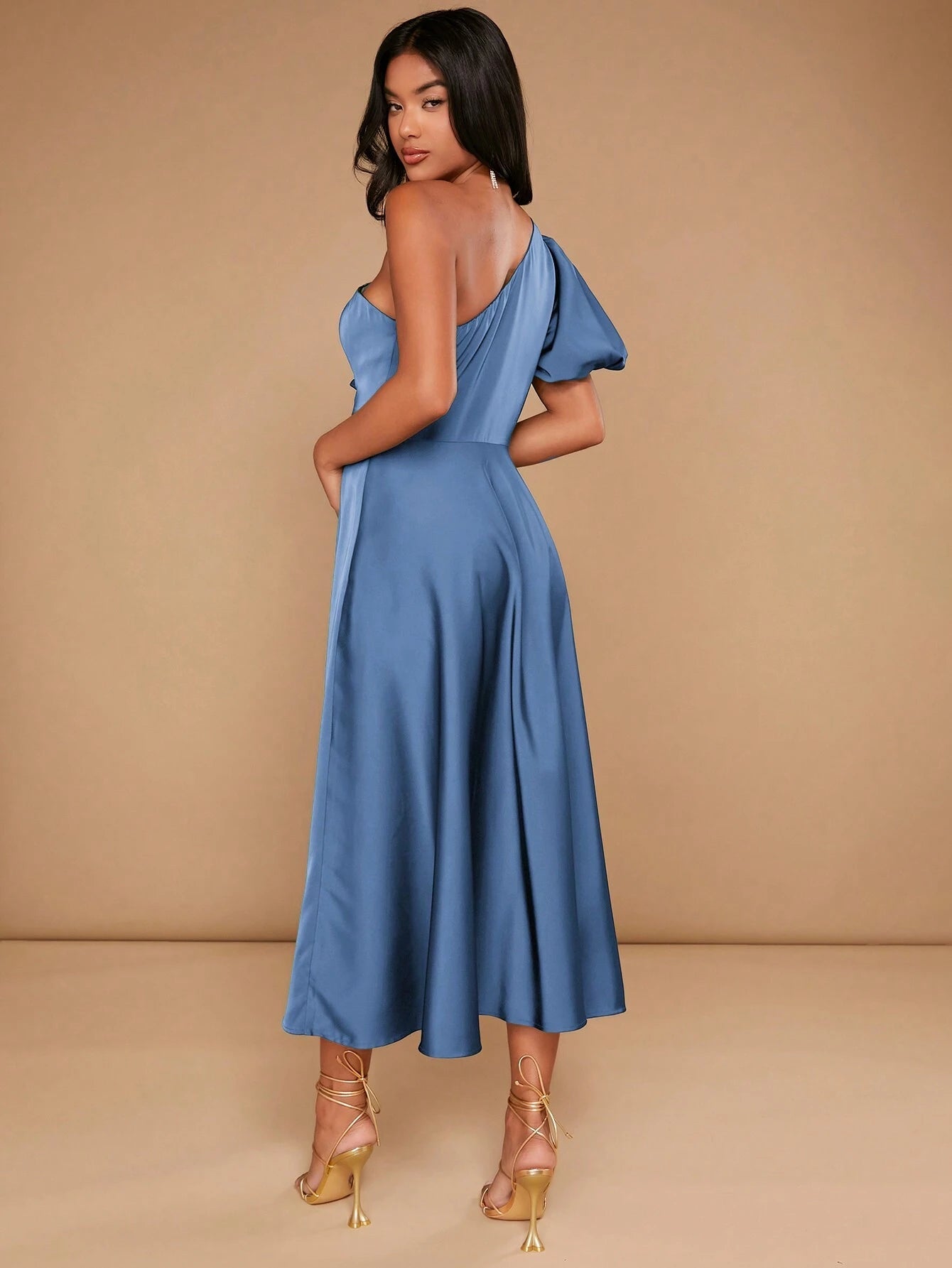 Vue de dos d'une élégante robe cocktail mariage bleu satinée, avec une coupe asymétrique à une épaule, portée par une femme dans un studio avec un fond beige.