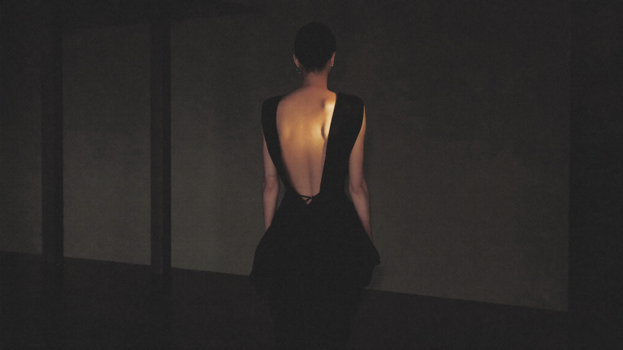 Robe cocktail noire dos nu dans une lumière dramatique — campagne Cocktail Chic