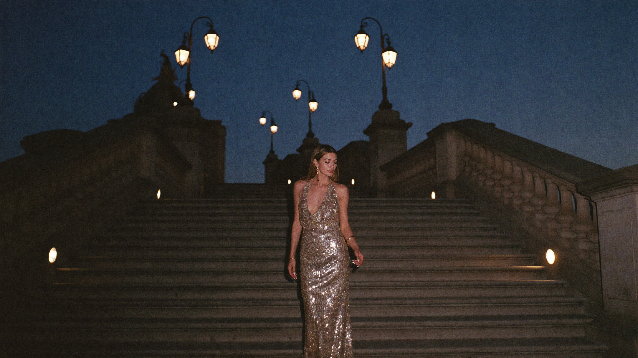 Robe cocktail champagne à sequins sur un escalier de pierre au crépuscule — campagne Cocktail Chic été 2026