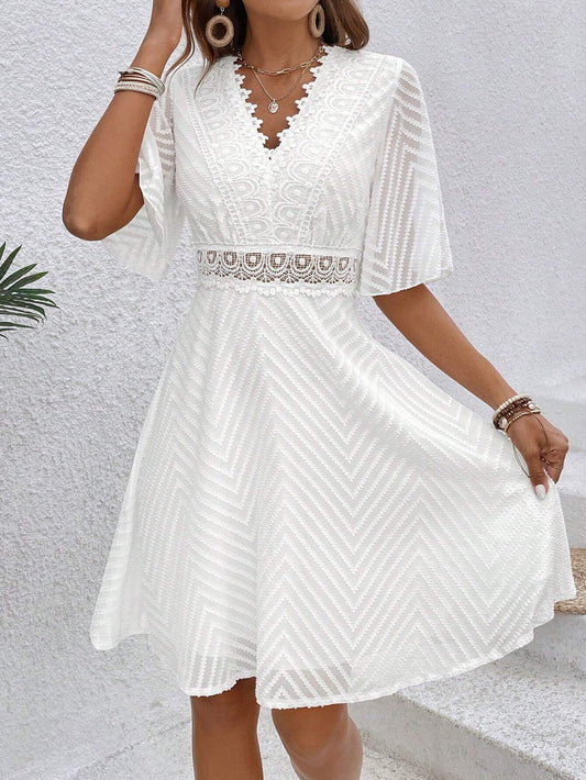 	Une robe cocktail blanche en dentelle bohème chic, vue de face, avec un décolleté en V et des manches évasées. La ceinture en dentelle accentue la taille, créant un look élégant et raffiné.