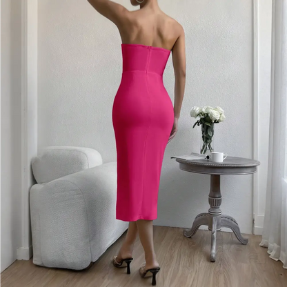 Vue de dos d’une femme portant une robe cocktail bustier rose fuchsia, debout à côté d’une table en bois.
