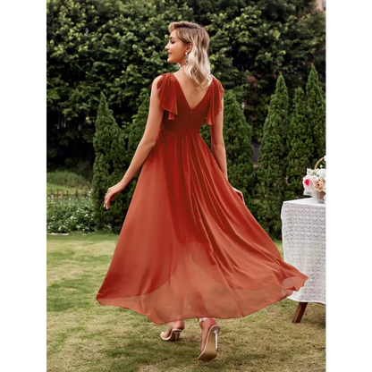 Vue de dos d'une élégante robe cocktail chic originale en terracotta, avec un décolleté en V et une coupe fluide, portée par une femme blonde dans un jardin verdoyant.