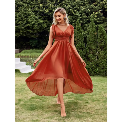 Vue de face d'une robe cocktail chic originale en terracotta, avec un décolleté en V et une coupe asymétrique, portée par une femme blonde dans un cadre extérieur élégant.