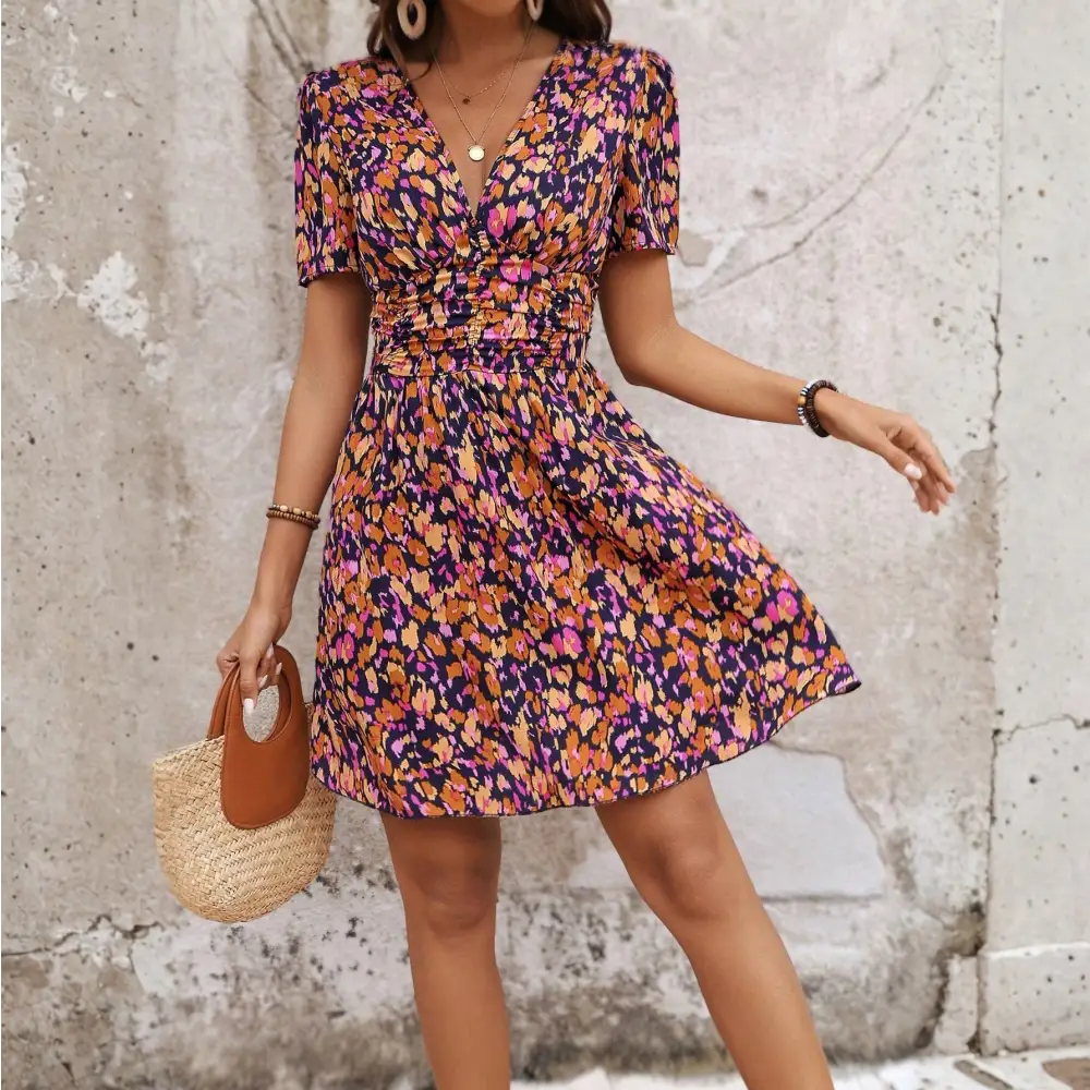 Vue de face d'une robe cocktail courte à motifs floraux colorés, avec un décolleté en V et des manches courtes, portée par une femme avec un chapeau de paille et un sac en paille.
