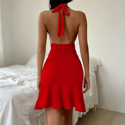 Femme portant une robe de cocktail dos nu vue de dos, avec une épaule dénudée et une coupe ajustée jusqu’aux chevilles, entourée de décorations florales élégantes.