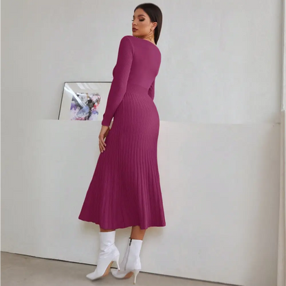 Vue de dos d’une femme portant une robe de cocktail hiver en tricot violet. La robe a des manches longues et une jupe plissée. La femme est accessoirisée avec des boucles d’oreilles dorées et des bottes blanches. Elle pose de dos, mettant en valeur la silhouette de la robe.