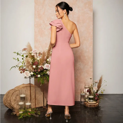 Vue arrière d'une femme portant une robe cocktail rose poudré, élégante et moderne, avec une épaule découverte et des volants sur l'épaule. La robe est ajustée pour mettre en valeur la silhouette et tombe jusqu'aux mollets, parfaite pour des occasions spéciales.
