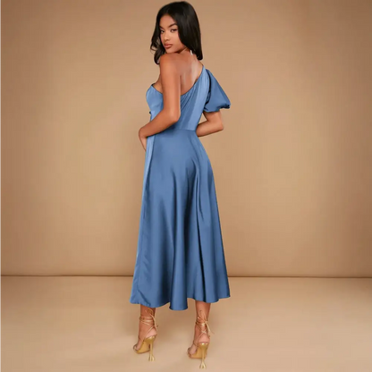 Vue de dos d'une élégante robe cocktail mariage bleu satinée, avec une coupe asymétrique à une épaule, portée par une femme dans un studio avec un fond beige.
