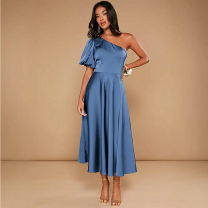 Vue de face d'une robe cocktail mariage bleu satinée, avec une épaule dénudée et une manche ballon, portée par une femme avec des sandales dorées.