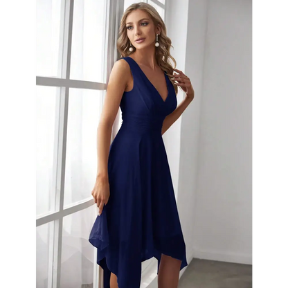 Femme portant une robe de cocktail bleue pour mariage, adossée à une fenêtre, vue de profil, montrant les détails plissés de la taille.