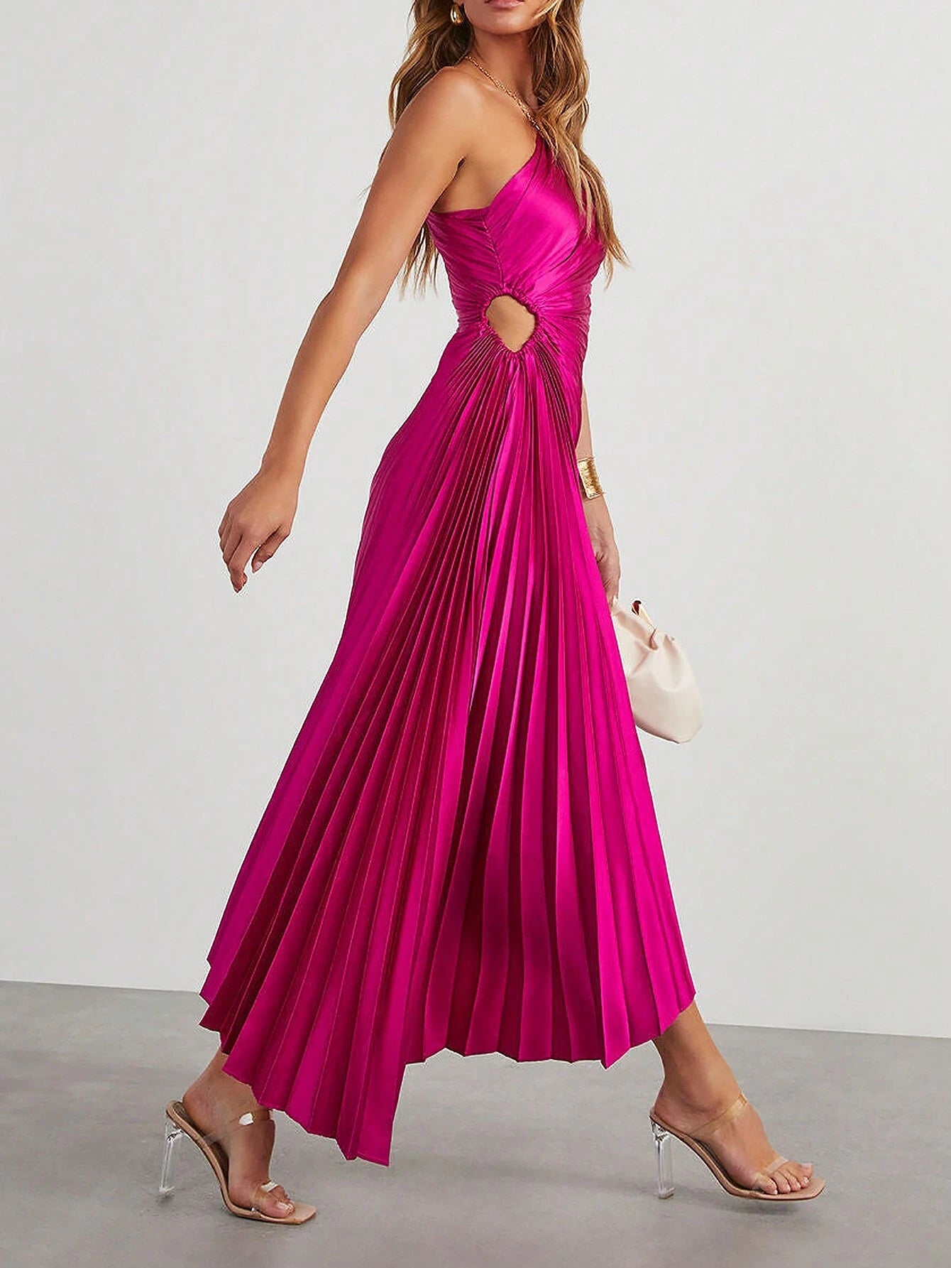 Une femme portant une robe cocktail satin de couleur fuchsia, en train de marcher. La robe est sans manches, présente des plis élégants et une coupe asymétrique avec une ouverture sur le côté de la taille.